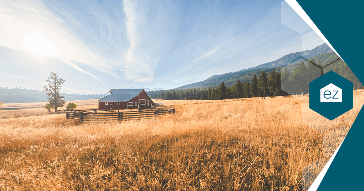 Rural Montana homestead with a red barn, open field, and mountains in the background