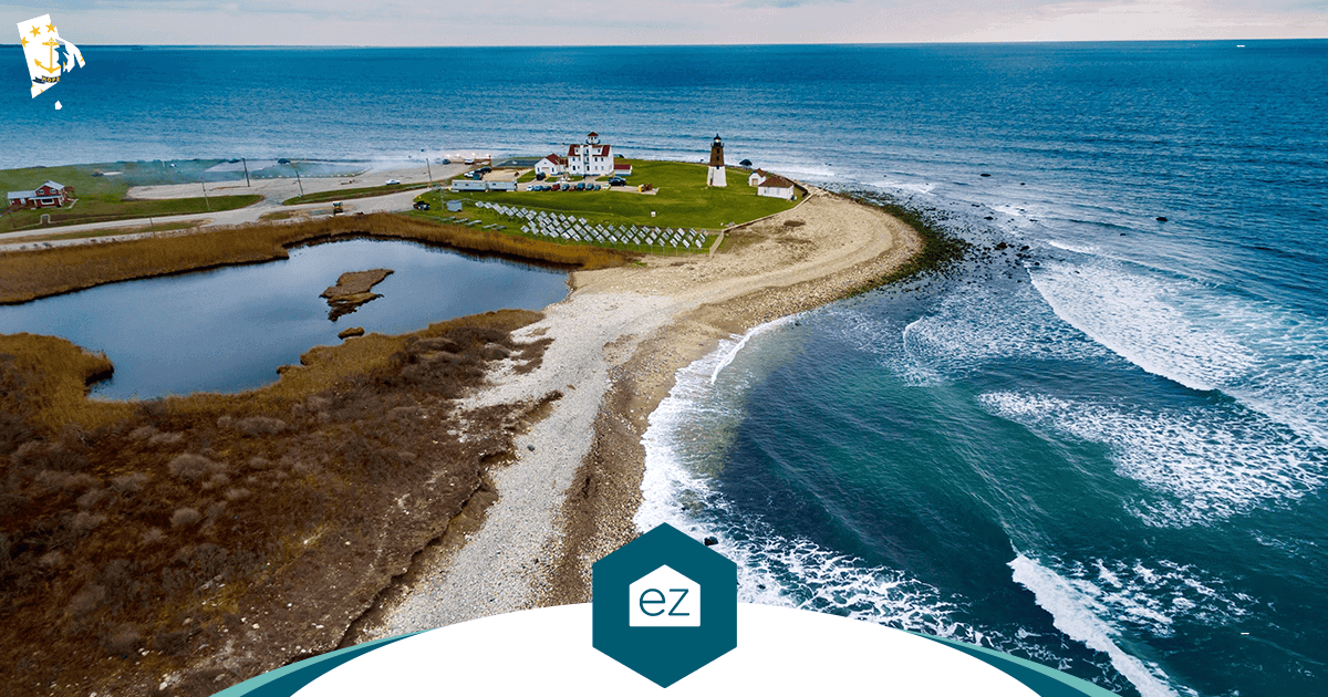 Aerial view of a lighthouse and buildings on a rocky Rhode Island peninsula bordered by ocean and a lagoon