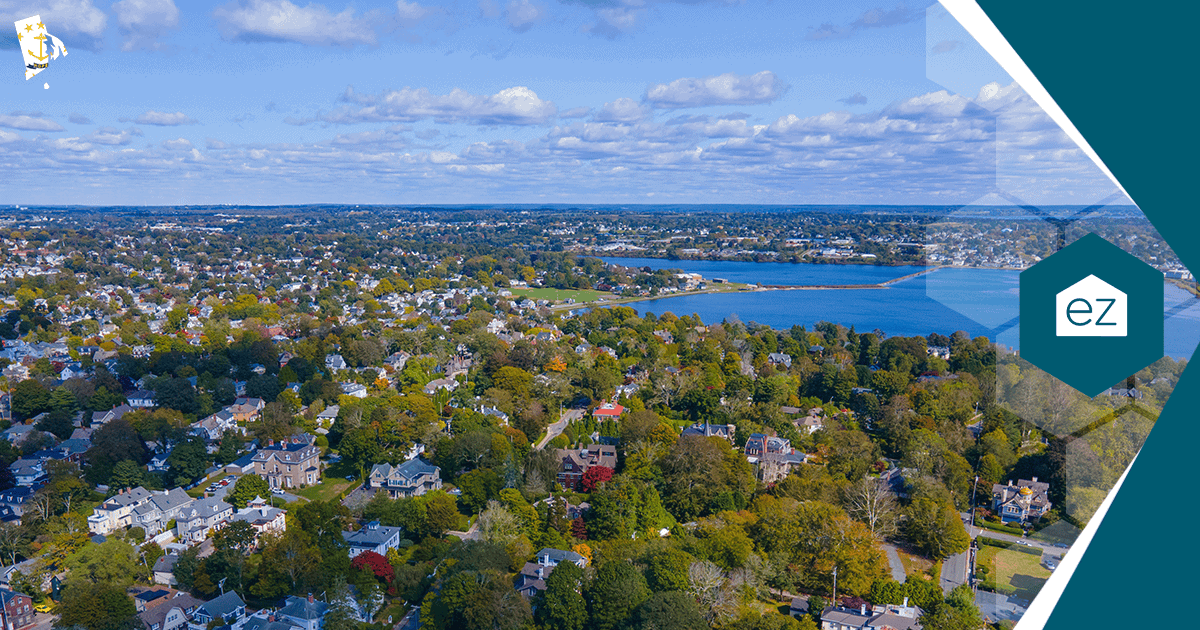 Aerial view of a Rhode Island coastal neighborhood with houses, trees and open water under a partly cloudy sky