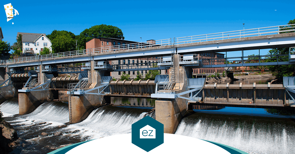 Water cascading over a dam spillway on a Rhode Island river with brick mill buildings behind it