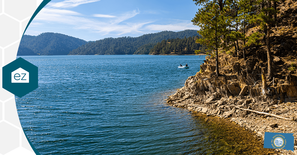 Two people in a small boat on a clear South Dakota lake bordered by forested hills