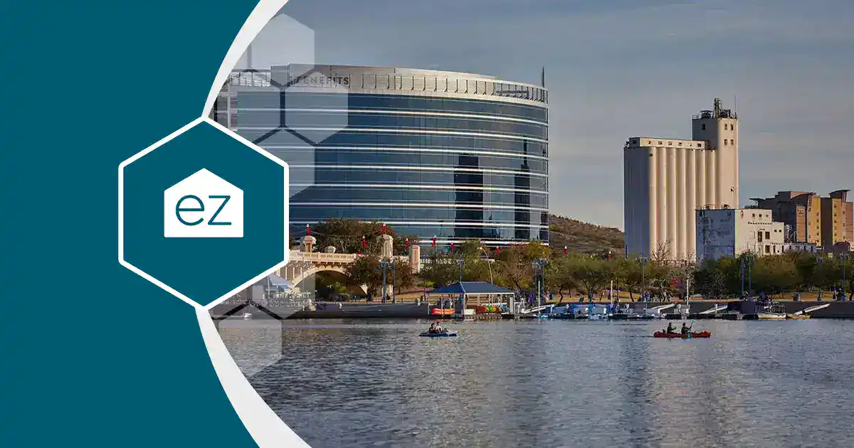 A modern glass office building and tall structures, part of the thriving Arizona real estate leads market, are seen across a river, with people kayaking on the water in the foreground.
