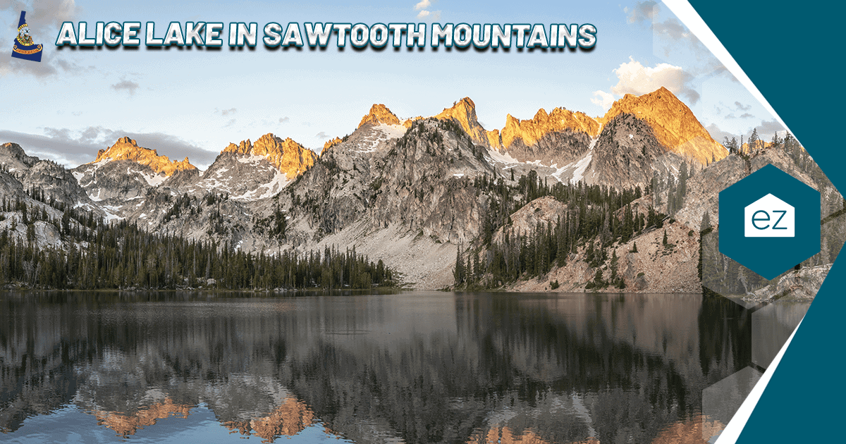 Alice Lake reflecting the rugged peaks of the Sawtooth Mountains at sunset, with pine trees along the shore in central Idaho
