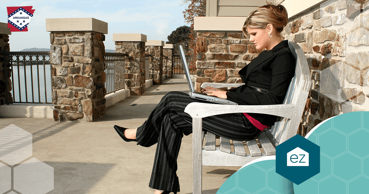 A woman in business attire working on a laptop on an outdoor bench overlooking water in Arkansas