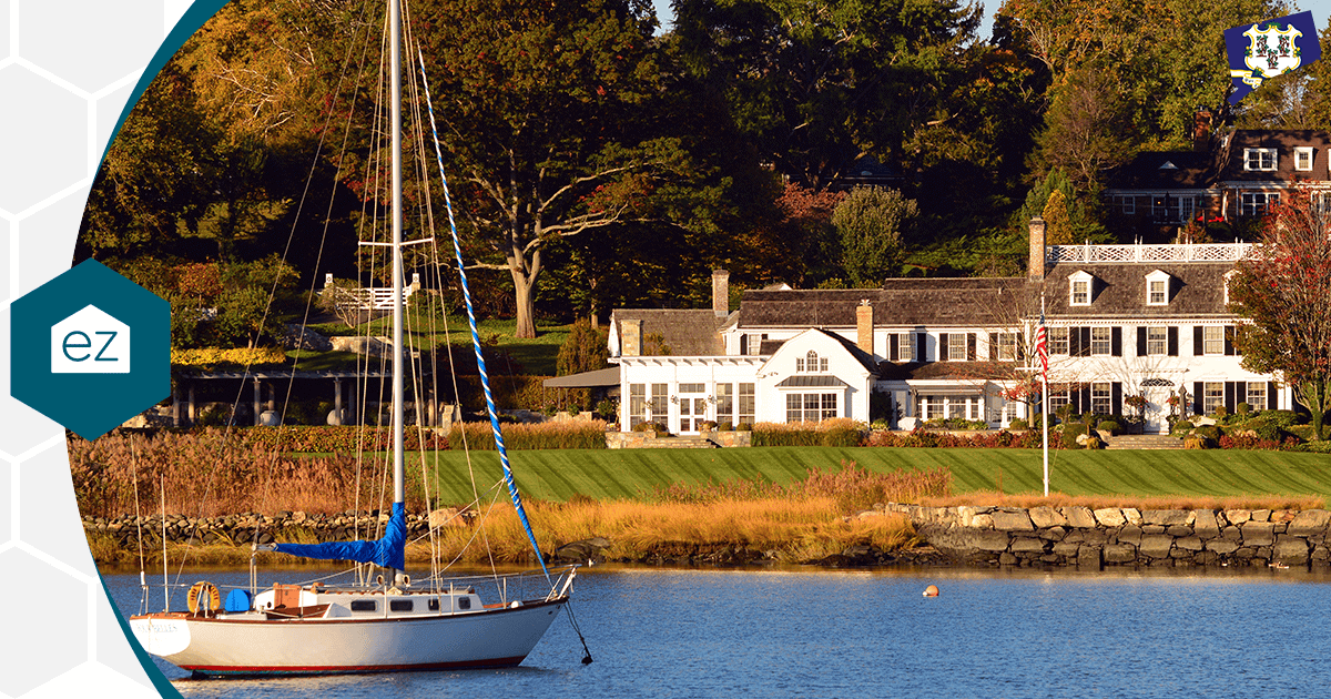 Waterfront Connecticut home with a sailboat and an American flag along a grassy shoreline
