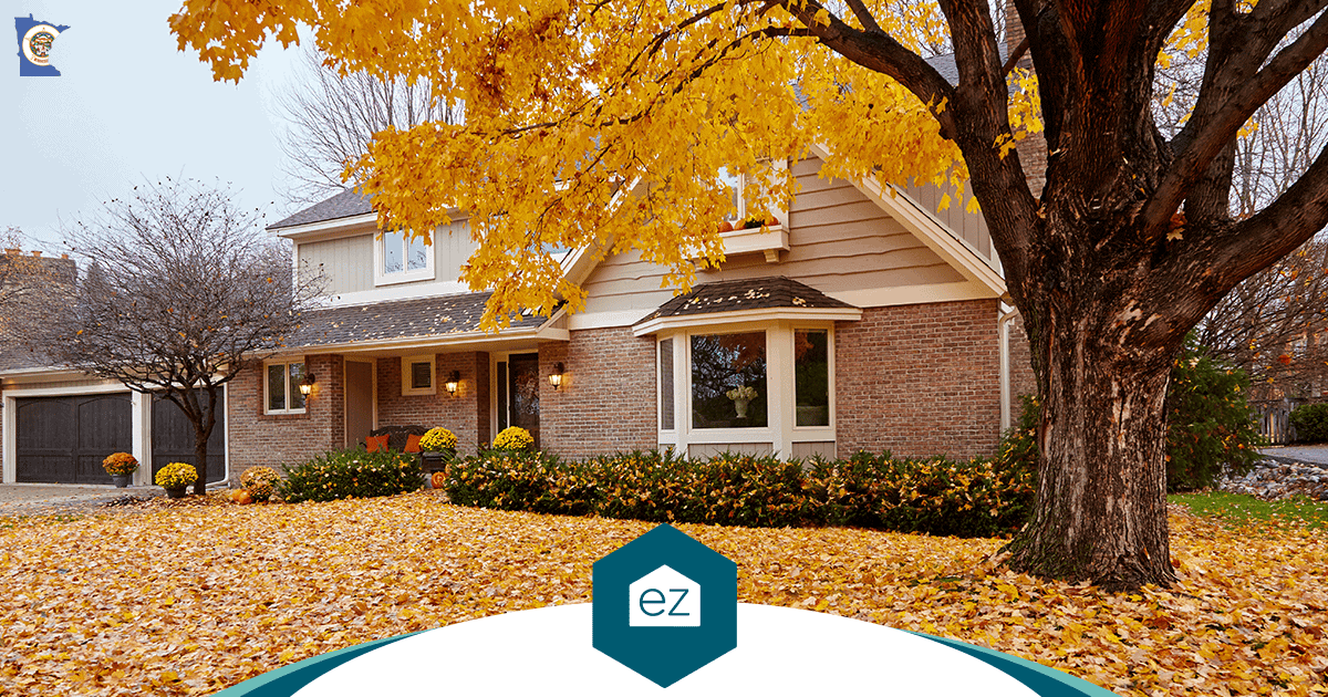 A two-story Minnesota home surrounded by autumn trees and fallen leaves