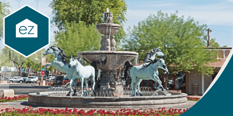 A stone fountain with four horse statues is in the center of a plaza surrounded by trees, flowers, and buildings—an inviting setting for Arizona real estate leads. A hexagonal "ez" logo appears in the corner on a sunny day.