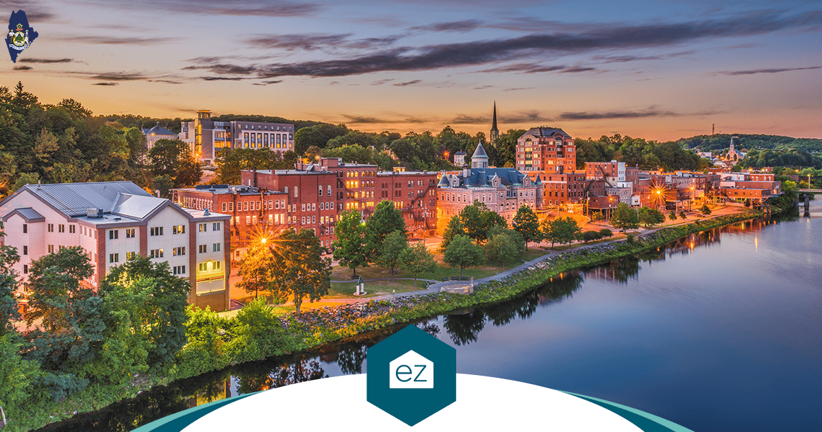 Historic brick buildings and a church spire along a Maine riverfront at sunset in a small coastal city