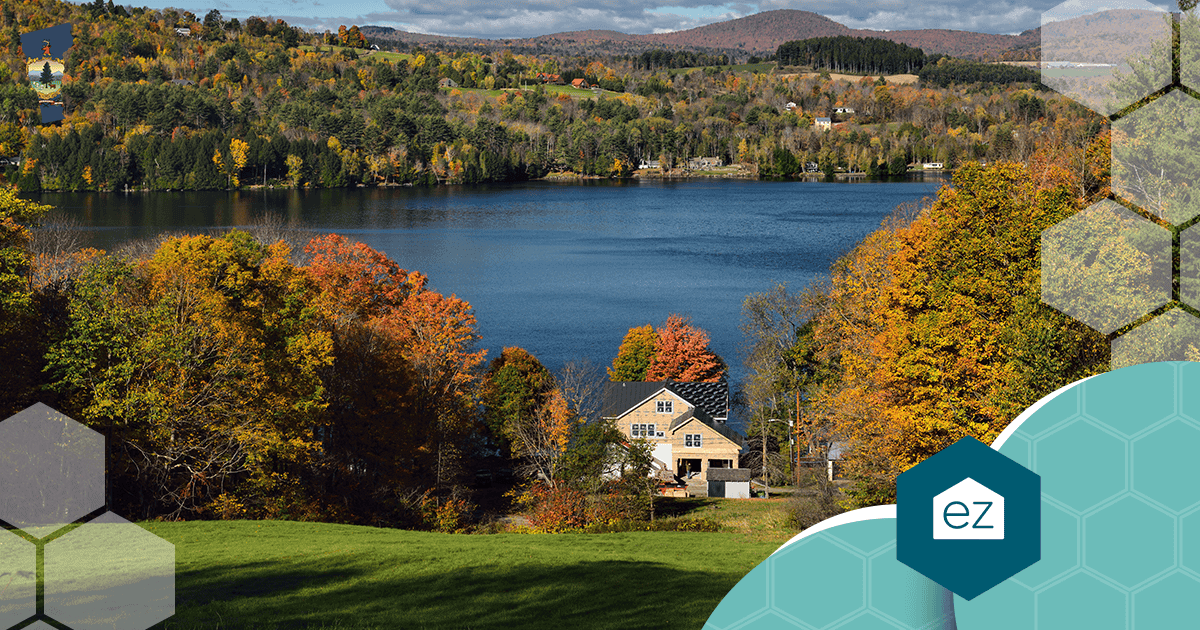 House under construction beside Harveys Lake in West Barnet, Vermont, surrounded by autumn trees and rolling hills