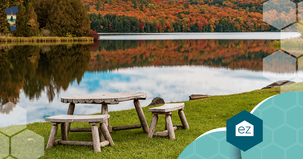 Wooden picnic table and benches on grass beside Silver Lake in Barnard, Vermont, with fall foliage reflecting in the water