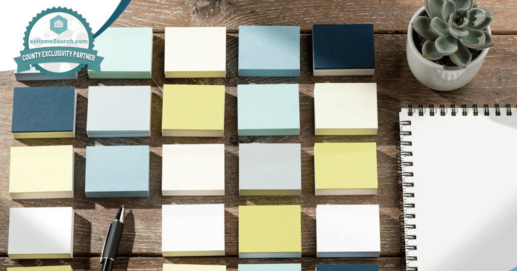 A grid of multicolored sticky notes is arranged on a wooden desk next to a notepad, pen, and a small potted succulent—an inviting workspace for anyone exploring how to nurture a real estate database with thoughtful planning and organization.