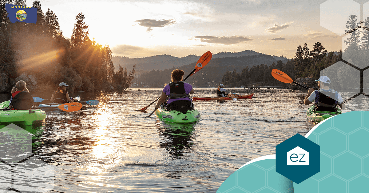 Kayakers paddling on a calm Montana lake at sunset, ringed by forested hills