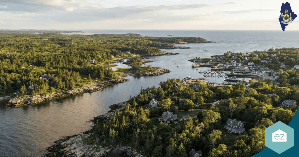 Aerial view of a coastal village with houses, trees, rocky shoreline, and a small harbor on a sunny day—an inviting scene ideal for generating Maine real estate leads.