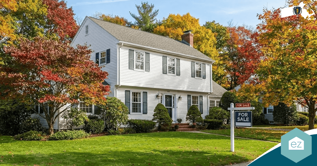 White two-story house with black shutters, surrounded by autumn trees, with a “For Sale” sign on the lawn. The sky is clear and the property appears well-maintained—an ideal opportunity for those seeking quality Massachusetts real estate leads.