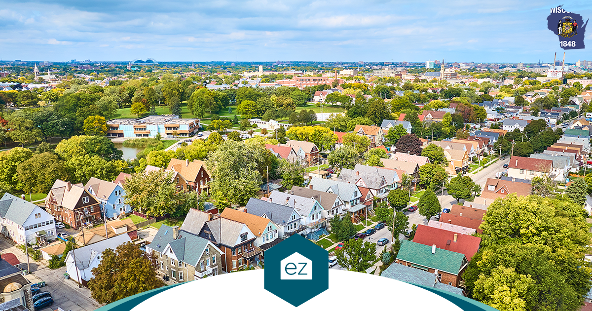 Aerial view of a Milwaukee County residential neighborhood with tree-lined streets and the downtown skyline beyond, the market behind Wisconsin real estate leads in the state's largest county