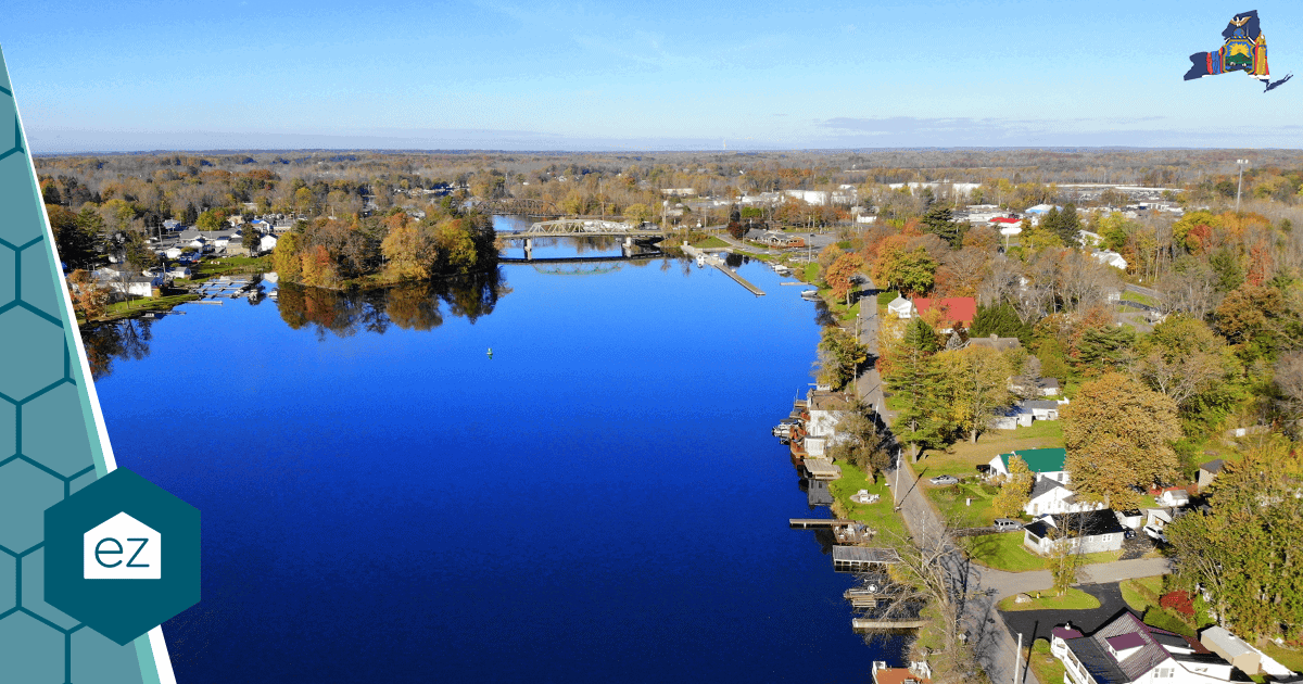 Aerial view of a New York river lined with houses and autumn trees, with a bridge in the background