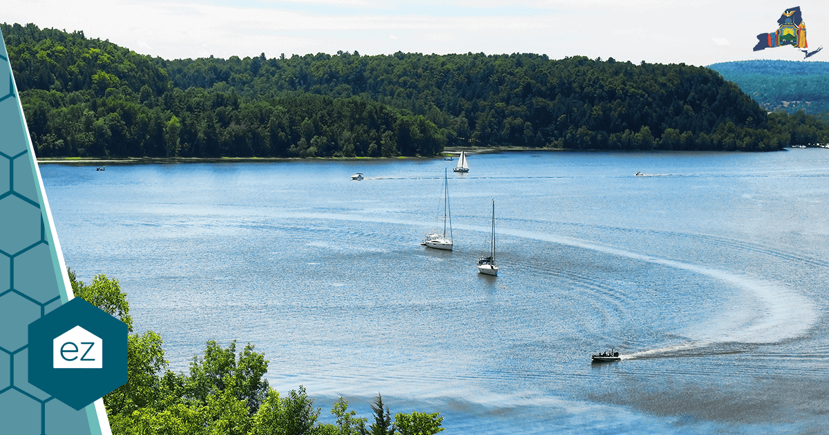 A New York lake with sailboats and a motorboat surrounded by dense forest