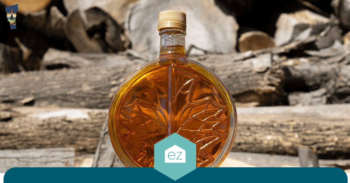 Maple-leaf shaped glass bottle of Vermont maple syrup in front of stacked firewood