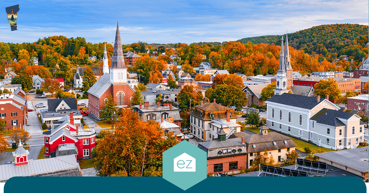 Aerial view of a small Vermont town with church steeples and houses surrounded by autumn foliage and wooded hills