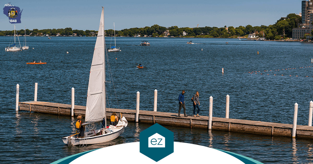 A sailboat approaching a wooden dock on a Wisconsin lake with people standing on the pier