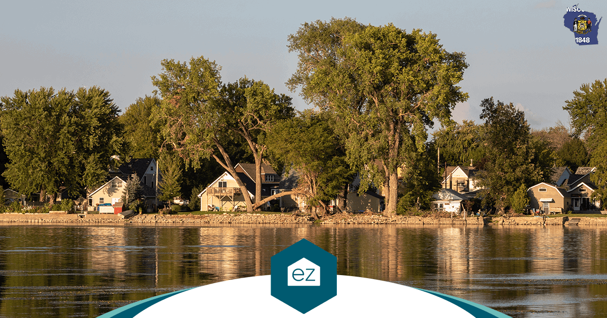A row of lakefront houses and large trees reflected in calm Wisconsin lake water