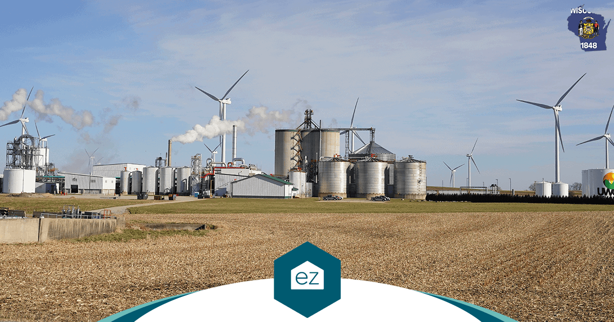 A Wisconsin manufacturing plant with wind turbines and storage tanks set against farmland, part of the employment picture moving Wisconsin households