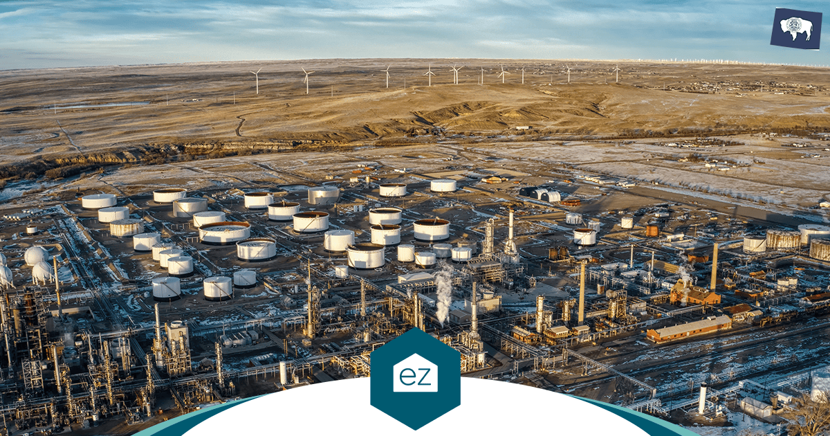 Aerial view of a Wyoming oil refinery with wind turbines on the horizon, part of the industrial construction pipeline driving housing demand across Sweetwater, Carbon, and Lincoln counties