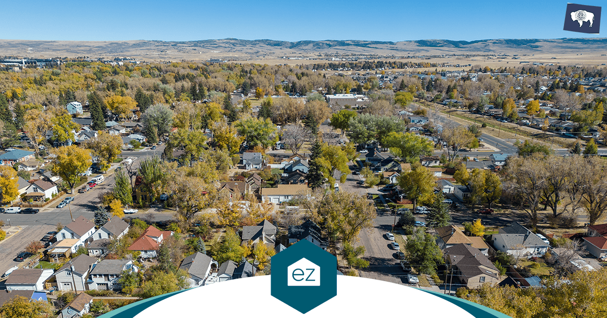 Aerial view of a small town with houses, trees, and roads, set against a backdrop of rolling hills under a clear blue sky—an inviting glimpse into the charm that draws buyers moving Wyoming in search of tranquil living and opportunity.